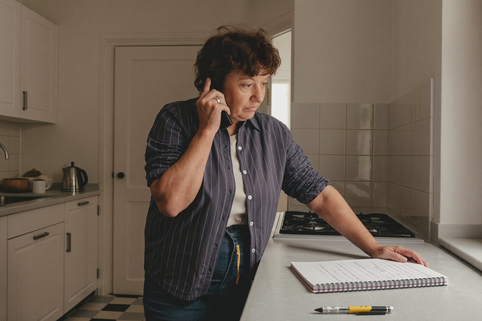 Frau am Küchentresen beim Telefonieren, Notizblock und Stift vor sich