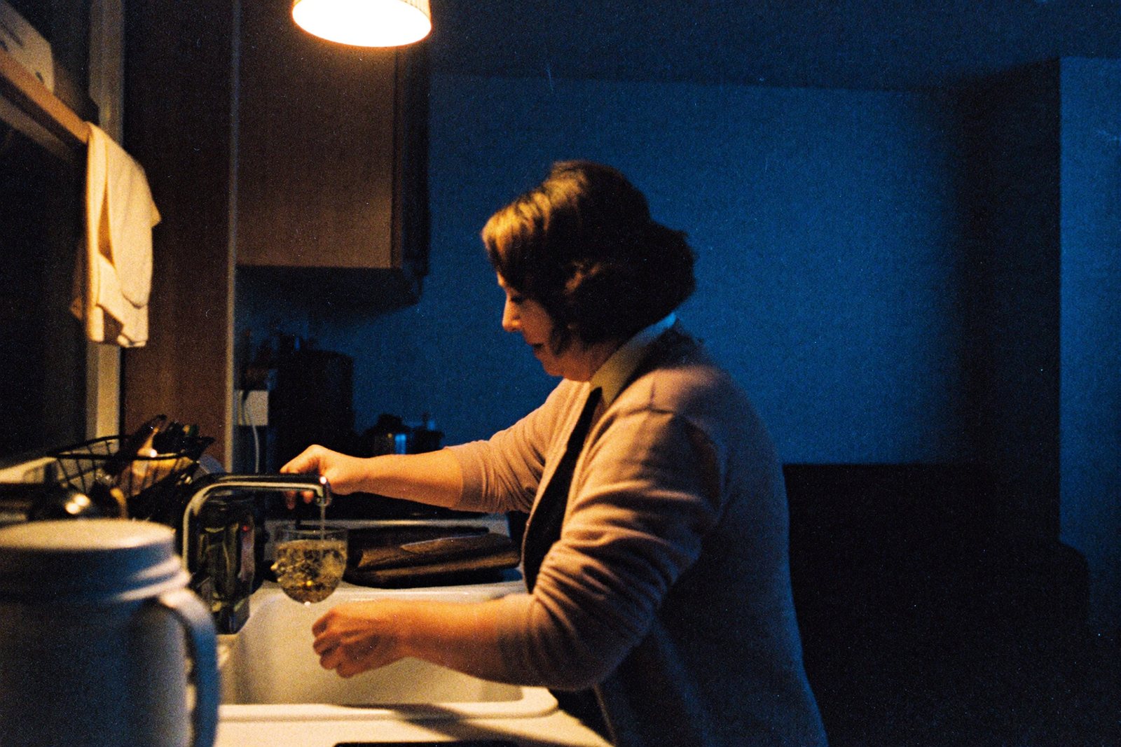 Küche bei Nacht, nur eine kleine Lampe brennt, eine Frau füllt ein Glas Wasser